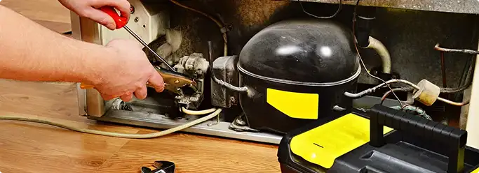 Refrigerator repair technician fixing the compressor and wiring in Liberty, MO