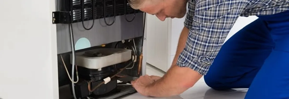Refrigerator repair technician servicing the compressor and condenser area in Kansas City, MO